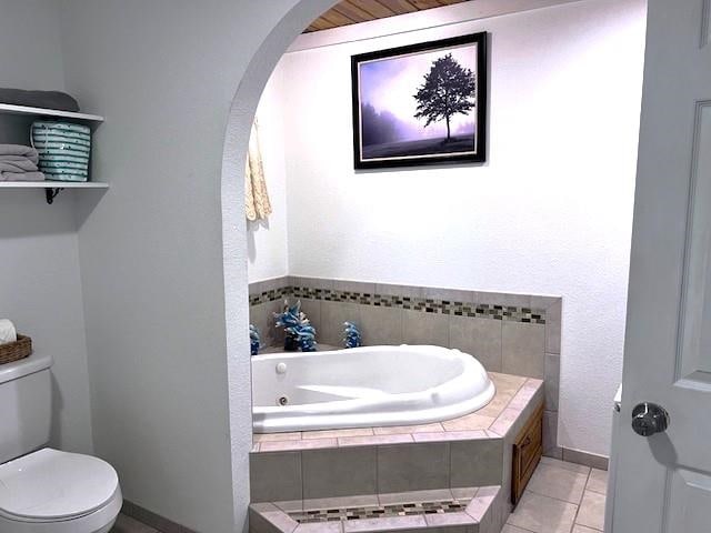 bathroom featuring tiled tub, toilet, and tile patterned flooring