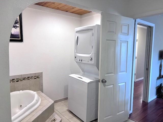 bathroom with tile patterned floors, stacked washer / dryer, wooden ceiling, and a relaxing tiled tub