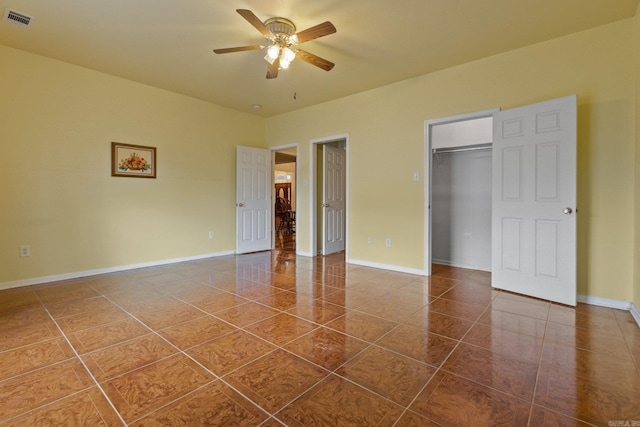 unfurnished bedroom featuring ceiling fan, a closet, dark tile patterned floors, and a walk in closet