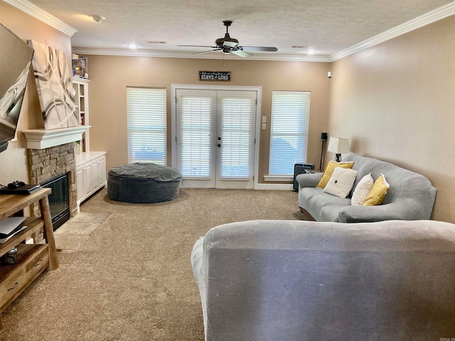 living room with a textured ceiling, light colored carpet, a stone fireplace, crown molding, and ceiling fan