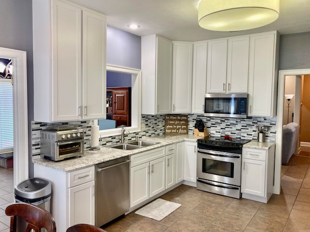 kitchen featuring sink, tasteful backsplash, white cabinetry, appliances with stainless steel finishes, and light stone countertops