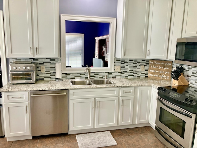 kitchen with white cabinets, appliances with stainless steel finishes, sink, and light stone countertops