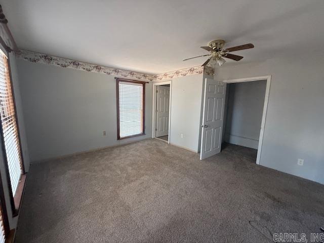 unfurnished bedroom with multiple windows, dark carpet, and ceiling fan