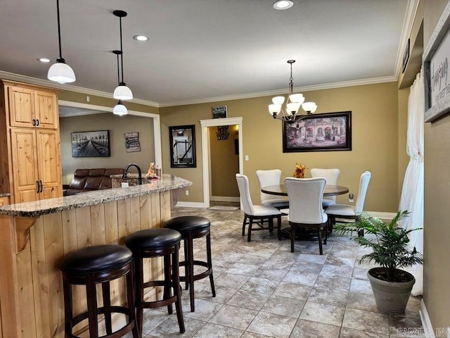 interior space featuring a breakfast bar area, pendant lighting, light brown cabinets, crown molding, and a chandelier