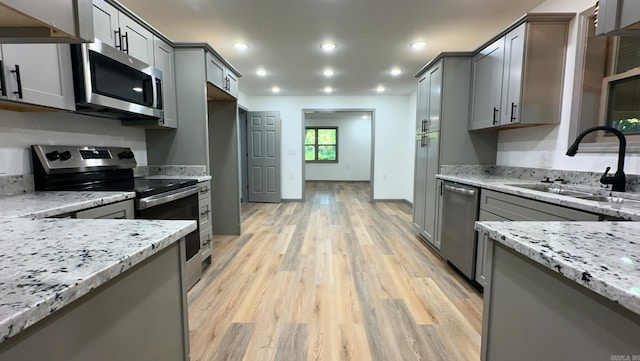 kitchen featuring light stone counters, light hardwood / wood-style floors, appliances with stainless steel finishes, and sink