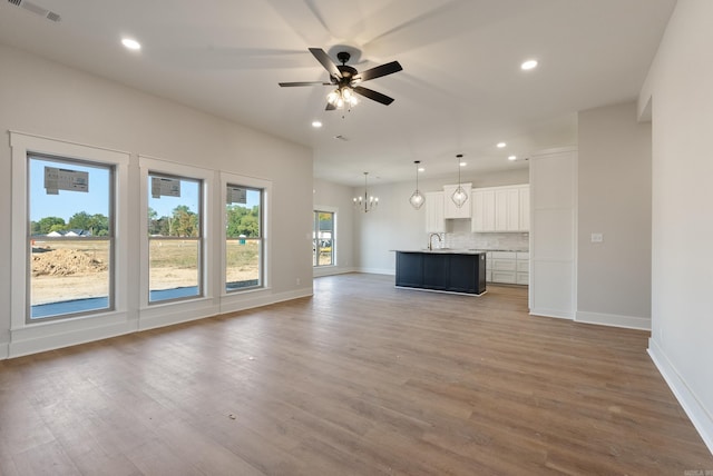 unfurnished living room featuring hardwood / wood-style flooring, sink, ceiling fan with notable chandelier, and plenty of natural light