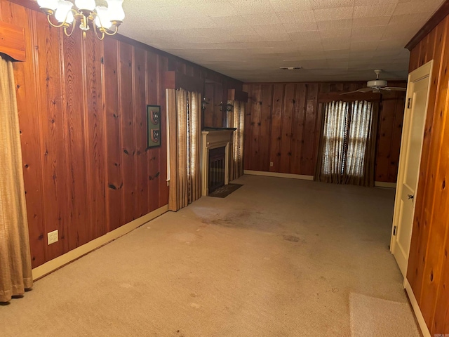 interior space with carpet floors, ceiling fan with notable chandelier, and wood walls