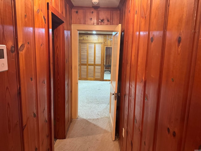 hall featuring light colored carpet and wooden walls