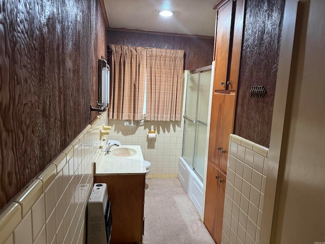 full bathroom with tile walls, heating unit, vanity, enclosed tub / shower combo, and toilet