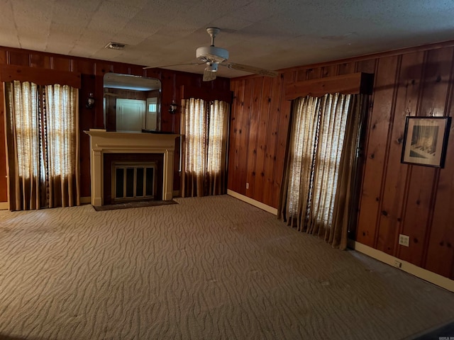 unfurnished living room featuring carpet floors, wood walls, and ceiling fan