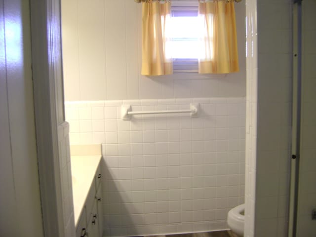 bathroom featuring vanity, tile walls, toilet, and a shower