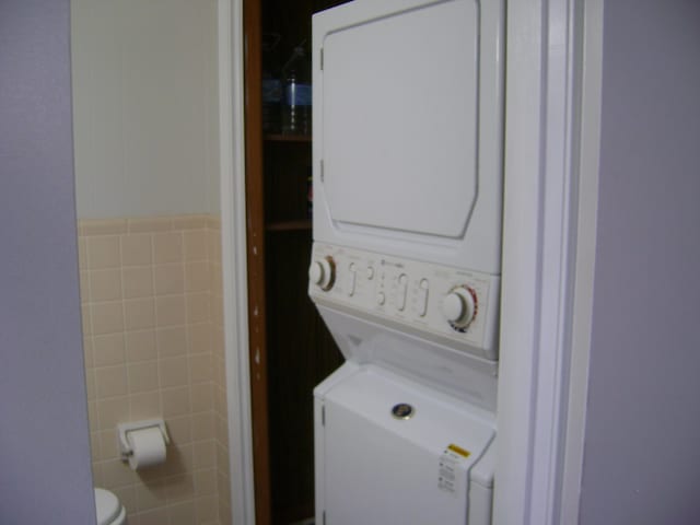 clothes washing area with tile walls and stacked washer and clothes dryer