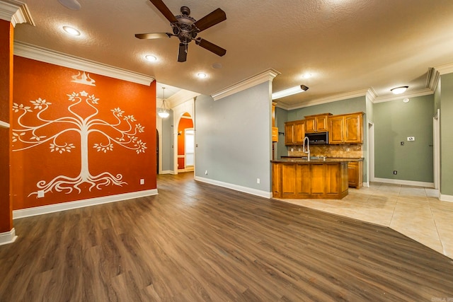 unfurnished living room featuring ceiling fan, sink, a textured ceiling, crown molding, and hardwood / wood-style floors