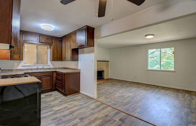 kitchen with ceiling fan, sink, dark brown cabinets, a brick fireplace, and light hardwood / wood-style flooring