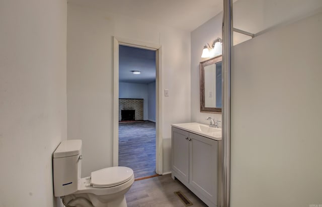 bathroom featuring wood-type flooring, a fireplace, vanity, and toilet