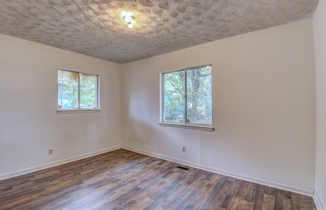 empty room with a textured ceiling, dark hardwood / wood-style floors, and a healthy amount of sunlight