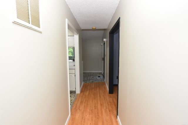 corridor with light hardwood / wood-style floors and a textured ceiling