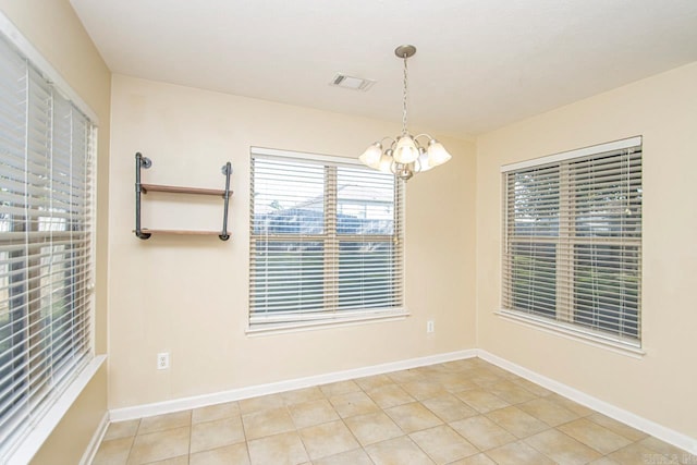 tiled spare room featuring an inviting chandelier