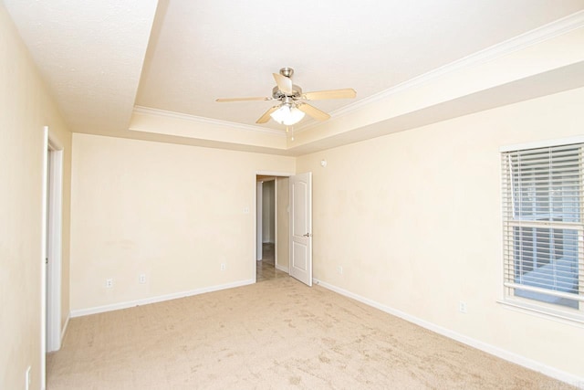 unfurnished room featuring a raised ceiling, ceiling fan, light colored carpet, and crown molding