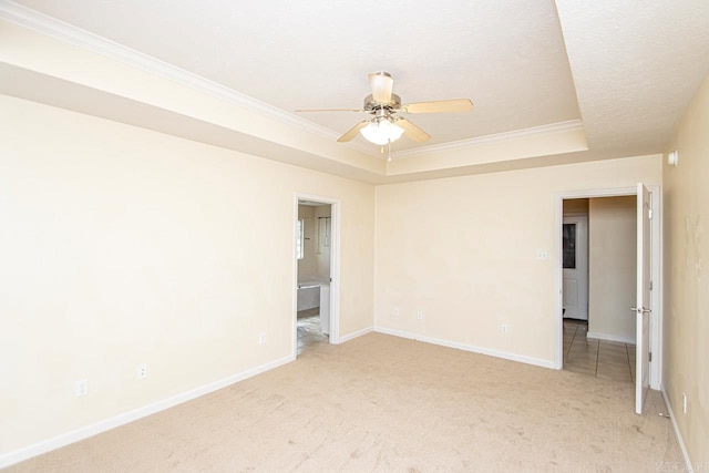 empty room with ceiling fan, a raised ceiling, light carpet, and crown molding