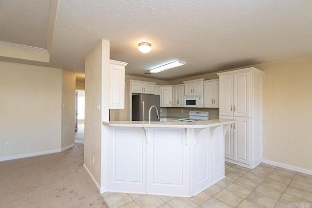 kitchen featuring white cabinets, light tile patterned floors, white appliances, a textured ceiling, and a breakfast bar area