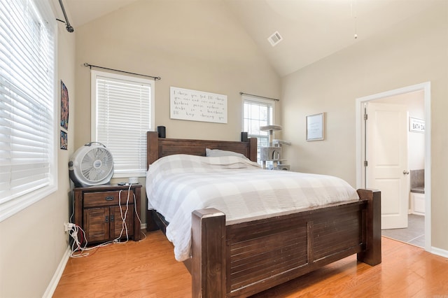 bedroom featuring connected bathroom, light hardwood / wood-style floors, and high vaulted ceiling