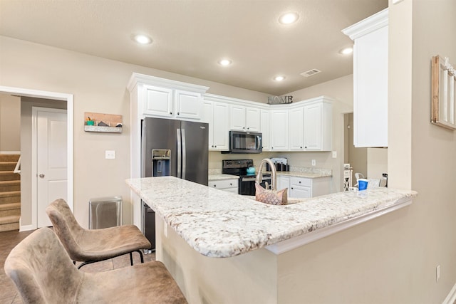 kitchen with light stone counters, white cabinetry, kitchen peninsula, a kitchen bar, and appliances with stainless steel finishes