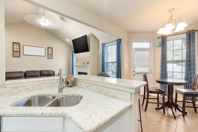 kitchen featuring light stone counters, lofted ceiling, sink, decorative light fixtures, and an inviting chandelier