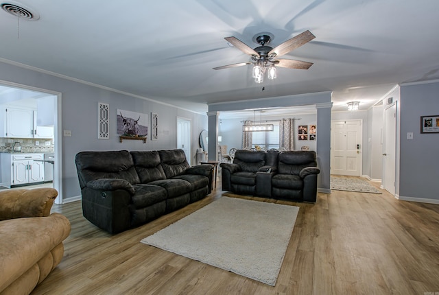 living room featuring light wood-type flooring, ceiling fan, crown molding, and ornate columns