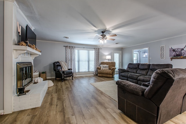 living room featuring light wood-type flooring, a fireplace, ornamental molding, and ceiling fan