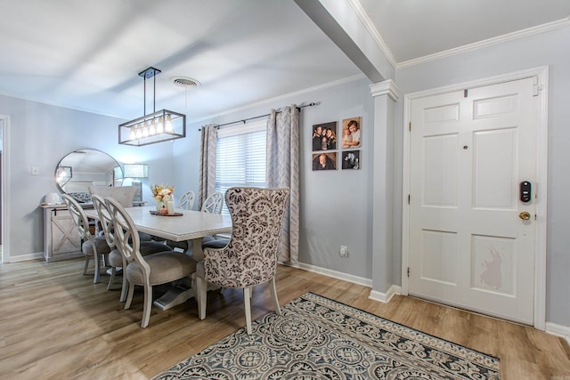 dining room featuring light wood-type flooring, crown molding, and ornate columns