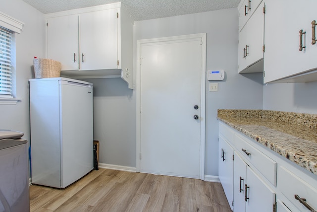 kitchen with light hardwood / wood-style floors, white cabinetry, white refrigerator, light stone countertops, and a textured ceiling