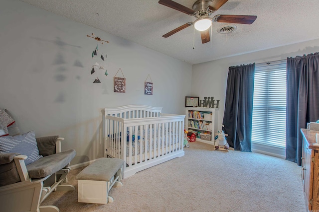 bedroom with a textured ceiling, a crib, light carpet, and ceiling fan