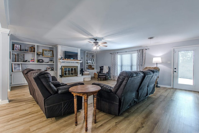 living room featuring light hardwood / wood-style flooring, a brick fireplace, ceiling fan, and built in features