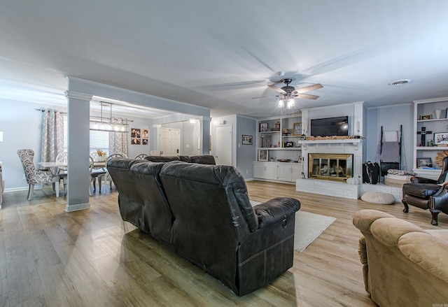 living room featuring light hardwood / wood-style floors, decorative columns, a brick fireplace, ceiling fan, and built in features