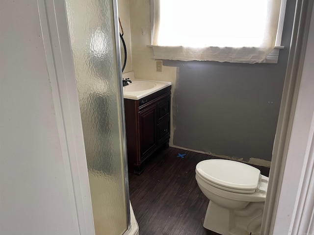 bathroom with wood-type flooring, a shower with shower door, vanity, and toilet