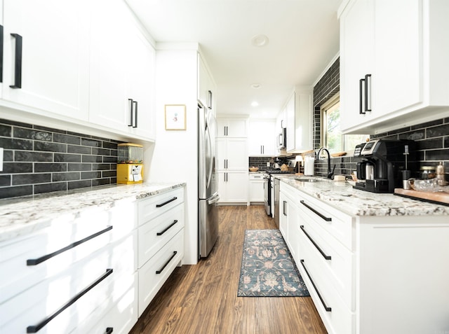 kitchen with appliances with stainless steel finishes, dark wood-type flooring, white cabinets, light stone countertops, and sink