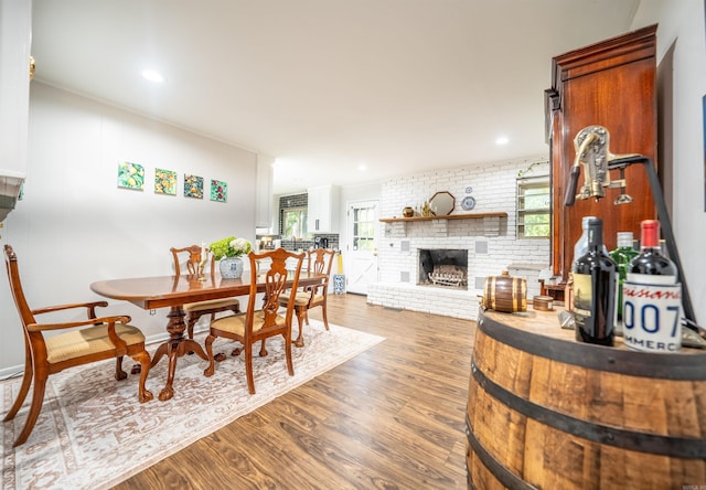 dining room with wood-type flooring, a fireplace, brick wall, and a healthy amount of sunlight