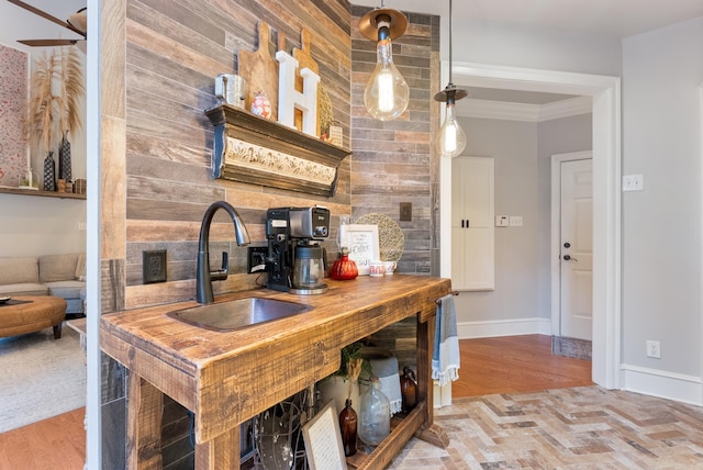 kitchen featuring hardwood / wood-style flooring, crown molding, decorative light fixtures, wooden walls, and sink