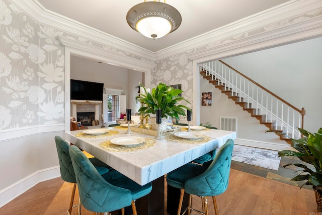 dining room featuring ornamental molding, a fireplace, and light hardwood / wood-style floors