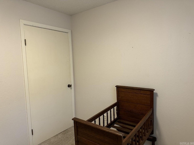 carpeted bedroom with a crib, a textured ceiling, and a closet