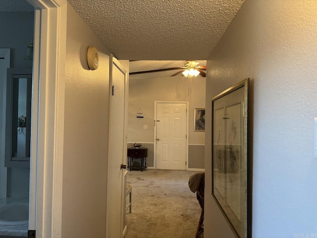 hallway featuring carpet floors, a textured ceiling, and vaulted ceiling