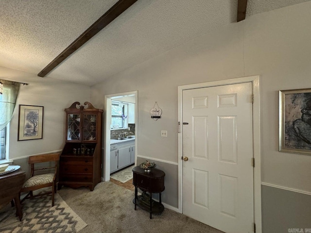 sitting room with light carpet, a textured ceiling, and lofted ceiling with beams