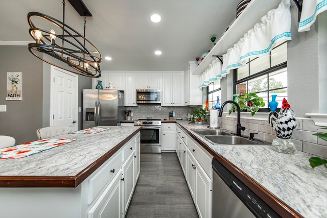 kitchen featuring appliances with stainless steel finishes, white cabinets, backsplash, sink, and a notable chandelier