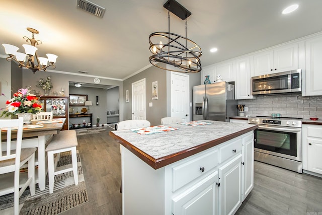 kitchen with appliances with stainless steel finishes, hanging light fixtures, white cabinets, and a notable chandelier