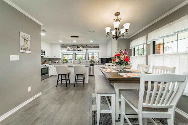 dining space with an inviting chandelier, light hardwood / wood-style floors, sink, and crown molding