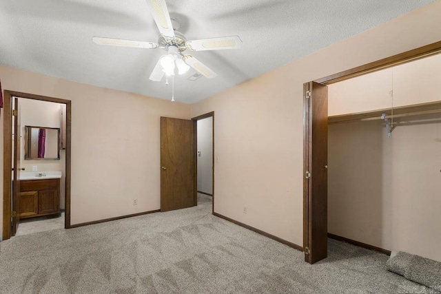 unfurnished bedroom with a closet, a textured ceiling, ceiling fan, ensuite bathroom, and light carpet