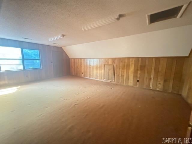 bonus room with a textured ceiling, wooden walls, and vaulted ceiling