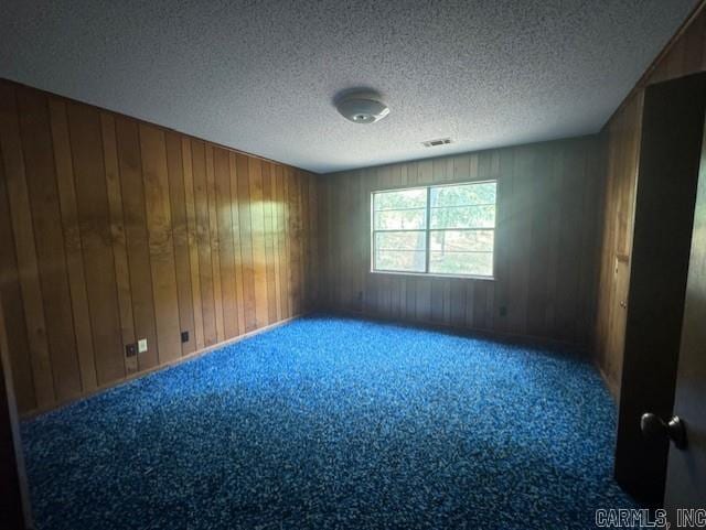 carpeted spare room with a textured ceiling and wood walls