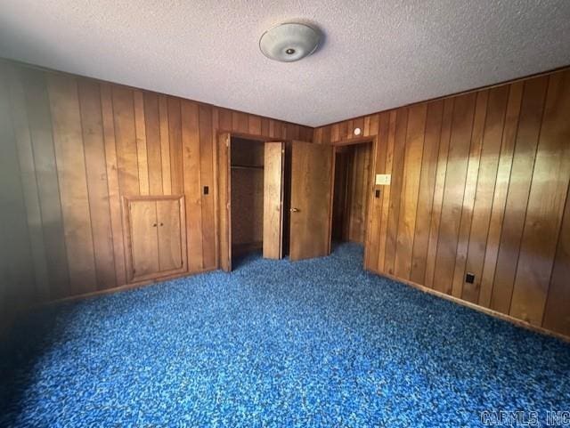 unfurnished bedroom with carpet, a closet, wood walls, and a textured ceiling